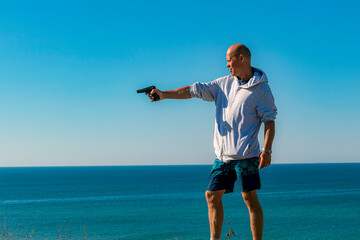 A man shoots a pistol at a target on the seashore.