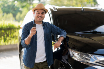 Young handsome asian man getting the new car.He showing car key and very happy. Buy or rent a car concept.