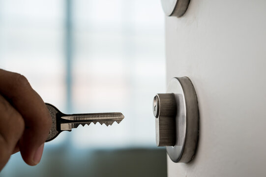 The man's hand was holding the key, trying to unlock the door. In order to enter the house. Home security concept.
