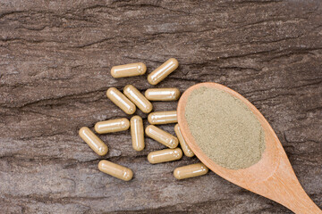Closeup green herbal powdercapsules pill in wooden spoon isolated on old wood table background. Top view. Flat lay.