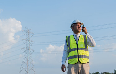 An Asian male engineer using a radio station is working in front of a high voltage pole. In the...