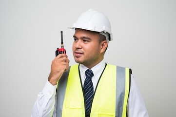Asian civil engineer operate with radio walkie talkie to control working in studio. Worker wearing hard hat standing on isolated white background.