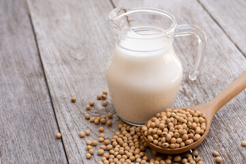 Selective focus. Soy bean in wooden spoon and soy milk in glass jar isolated on wood table background.