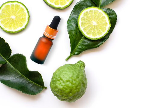 Green Bergamot or kaffir lime fruit with cut in half and bottle of essential bergamot oil extract isolated on white background. Hair tonic concept. Top view. Flat lay.