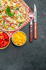 top view of bowl of vegetable salad on red napkin with veggies and cutleries on side and with free place for text in the bottom on dark table