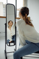 Obraz premium Photo portrait of young woman looking at mirror reflection wearing casual clothes sitting in front of window