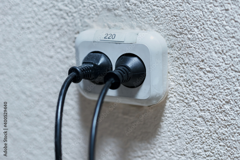 Wall mural old white plastic double socket with two black dirty cords indoor.