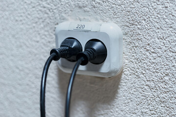 Old white plastic double socket with two black dirty cords indoor.