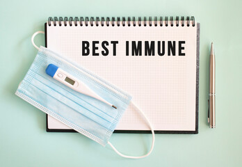 A medical protective mask and a thermometer are on the notepad. BEST IMMUNE text in a notebook.