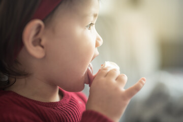 A toddler sitting on a sofa sticks her tongue out to lick a bun while her pinkie sticking up in a...