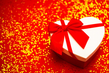 A gift for a loved one in the shape of a heart for Valentine's Day. Festive background with sparkles and red ribbon. Surprise on a red background.