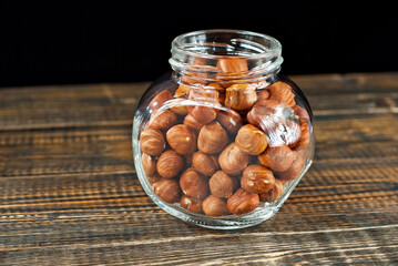 Hazelnuts peeled in a transparent glass jar. Nuts on an old shabby board. Jar on a brown wooden table close up.