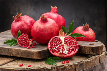 Healthy pomegranate fruit with leaves and open pomegranate on an old wooden board, side view, dark vintage background. - obrazy, fototapety, plakaty