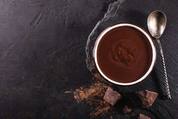 Melted chocolate in a bowl and chunks of dark chocolate on a slate board, top view, copy space.