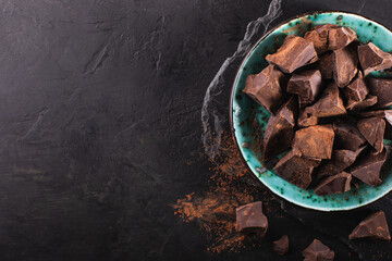 Pieces of bitter organic chocolate in a vintage bowl on a dark textured background, top view, copy space. Confectionery chocolate background.