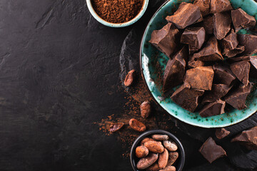 Organic broken chocolate in a vintage bowl, cocoa beans and cocoa powders on a dark textured...
