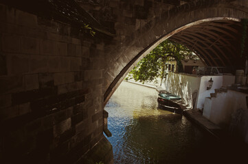 Fototapeta na wymiar Czech Republic, Prague. An old boat stands under a stone historic bridge in the sun.