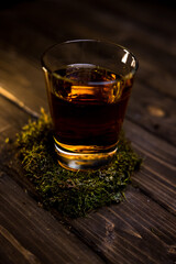a glass of whiskey  with moss on a wooden table 
