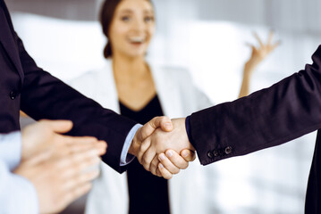 Businessmen are shaking hands while standing with colleagues applauding in office, close-up. Business success concept