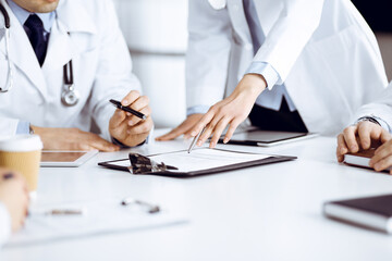 Group of unknown doctors are sitting at the desk and discussing medical treatment, using a clipboard, close-up. Team of physicians at work in a clinic. Medicine and healthcare concept