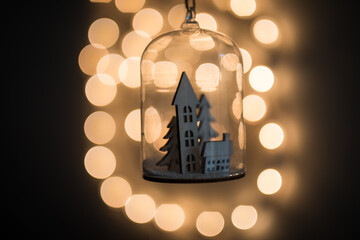 A glass enclosed dome globe with small house village inside against blurred christmas lights