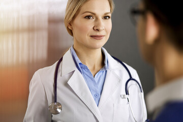 Friendly female doctor and patient man discussing current health examination while sitting in sunny...