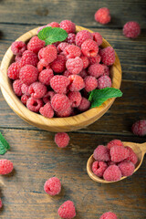 Fresh raspberries in a wooden plate with leaves. The berries are scattered on a wooden table.