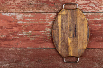 Empty oval cutting board with iron handles on a red wooden table.