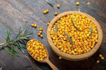 Sea buckthorn with leaves in a wooden bowl on a wooden table.
