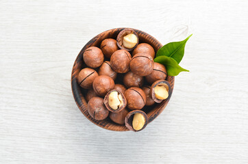 Macadamia nut in bowl on white wooden background.