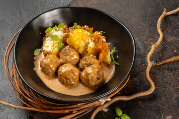 Meatballs with gravy and baked potato garnish. A hot main course in a beautiful black plate.