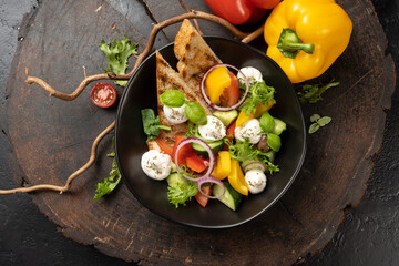 Vegetarian salad of vegetables, onions, cherry tomatoes, red and yellow bell peppers and greens with mozzarella cheese. Fresh summer salad appetizer.