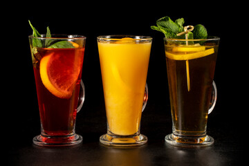 A set of three hot tea drinks with lemon and freshly squeezed orange juice. Hot warming drinks on a black background. Hot cocktails for winter holidays