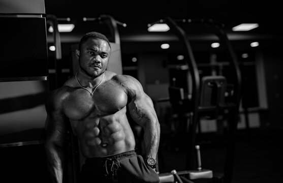 Brutal strong bodybuilder posing on modern gym background. Strong body and perfect abs. Black and white photo.