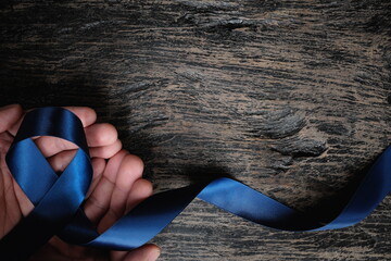 Top view of male hand holding dark blue ribbon on wooden background with copy space. Colon,...