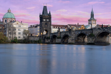 Fototapeta na wymiar Charles Bridge on the Vltava River at sunset and colorful clouds and lights on the bridge in the early evening in the center of Prague