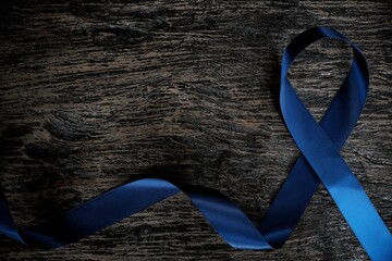 Top view of dark blue ribbon on wooden background with copy space. Colon, stomach, colorectal cancer, arthritis awareness and child abuse prevention concept.