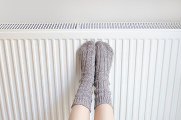 Woman is warm knitted woolen socks near a home heater in cold winter time. Using heater at home in...