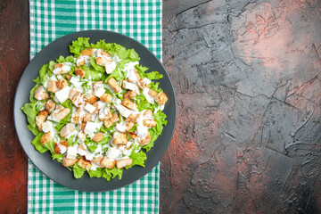 top view caesar salad on oval plate green white checkered tablecloth on dark red background with free place