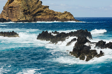 Rocky ocean shore. Sea wave background. Rocky cliff Madeira island landscape. Water foam on the surface. Turbulent ocean hitting the shore. Madeira rocky shore. Lava pools landscape.