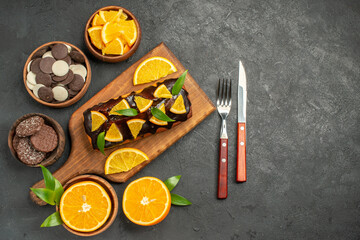 Obraz na płótnie Canvas Soft cakes on wooden cutting board and cut lemons with leaves biscuits on dark background