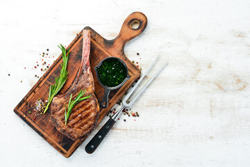 Tamahavk steak on the bone with spices and herbs. On a white wooden background. Top view. Free copy...