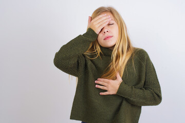Fototapeta premium Caucasian kid girl wearing green knitted sweater against white wall Touching forehead for illness and fever, flu and cold, virus sick.