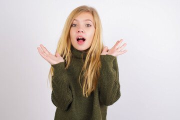 Surprised terrified Caucasian kid girl wearing green knitted sweater  Gestures with uncertainty,...
