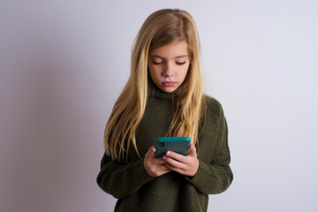 Excited Caucasian kid girl wearing green knitted sweater against white wall  winking and eye hold...