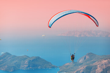 Instructor and student in tandem soar in the air on a large blue paraglider. Mountains and sea in the background. Positive and sharp impressions for tourists