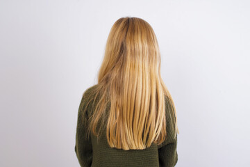 The back view of a Caucasian kid girl wearing green knitted sweater against white wall . Studio Shoot.