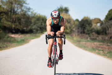 Cyclist with helmet and sunglasses riding in the middle of a rural road on a sunny day
