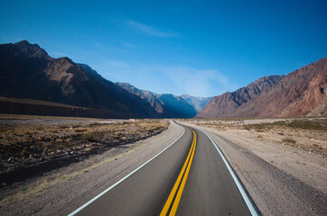 Empty asphalt highway road with curves and yellow dividing line in a desert valley in Andes Mountains - Mendoza province - Argentina