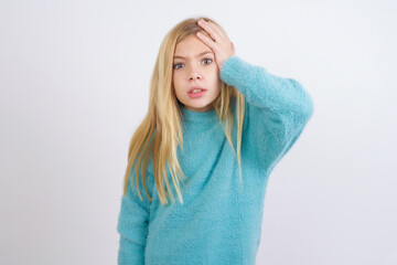 Portrait of confused Cute Caucasian kid girl wearing blue knitted sweater against white wall...